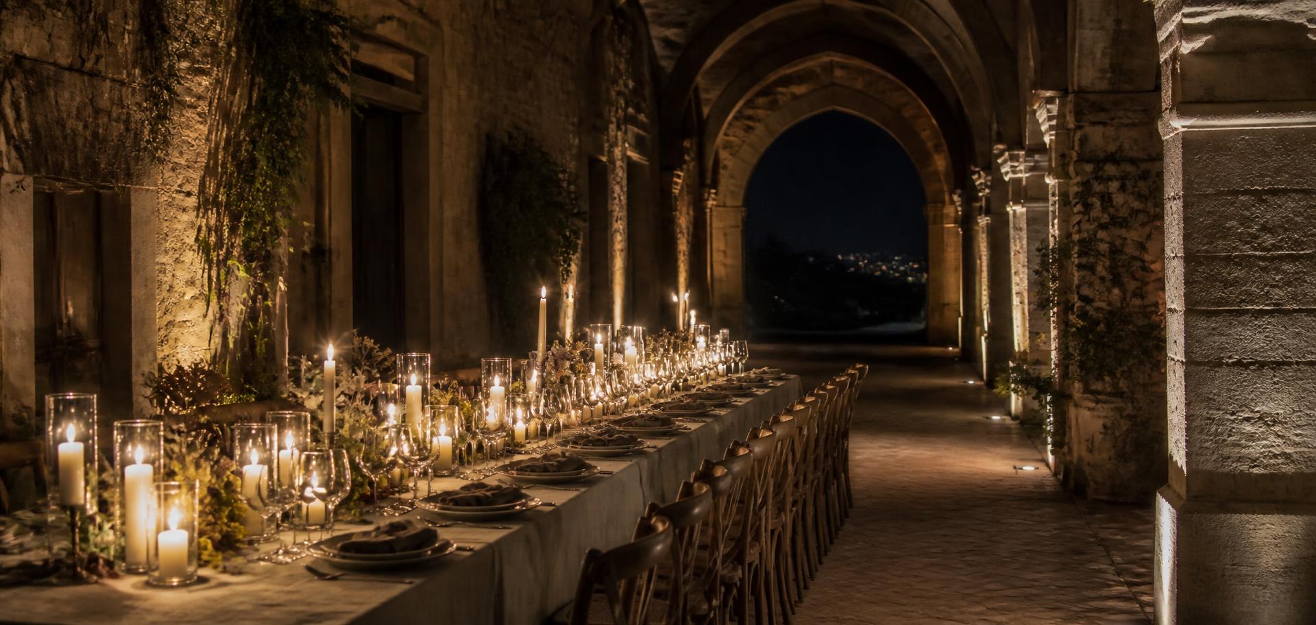 Mesa iluminada por velas sob arcadas de pedra à noite